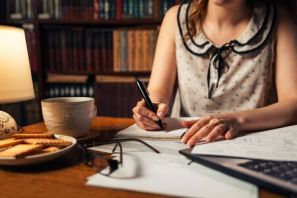 143936716-una-mujer-joven-está-sentada-en-una-mesa-trabajando-con-documentos-y-escribiendo-algo-en-la-mesa